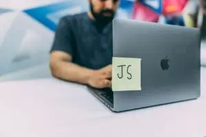 Man typing on laptop with JavaScript post-it note attached